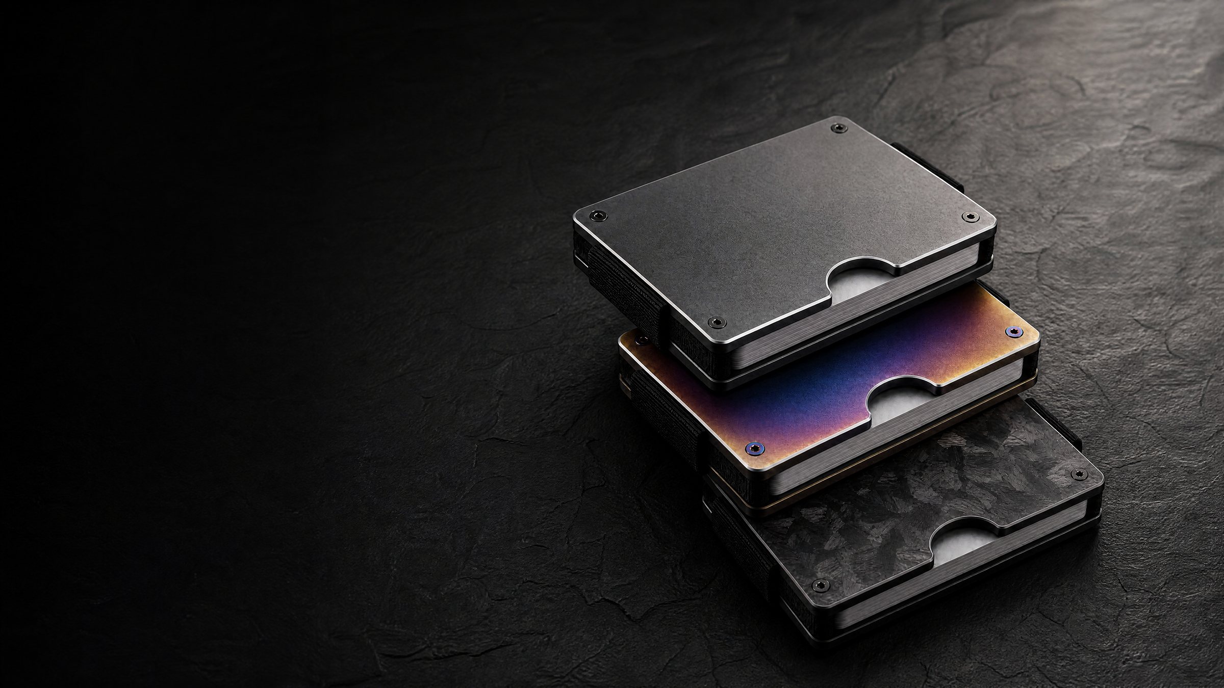 An ANODE metal card wallet resting on a dark stone surface, lit from the side